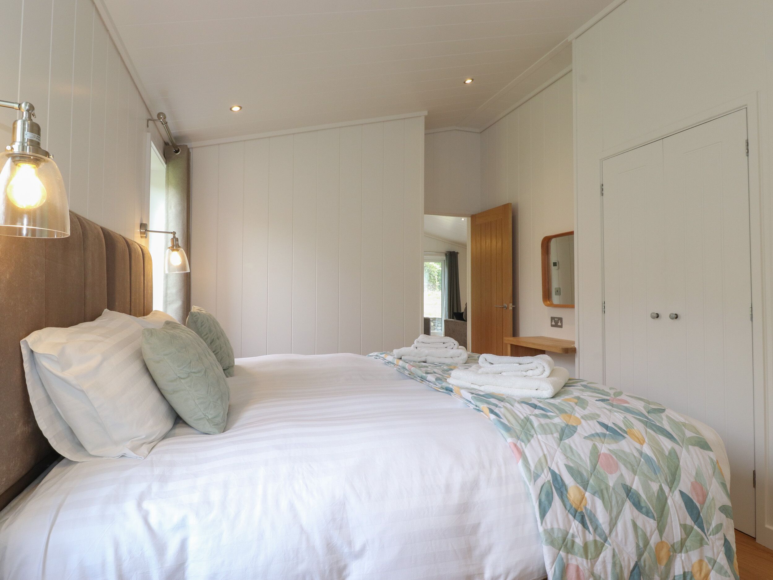 Quarto com uma cama grande, cabeceira de madeira, mesa de cabeceira, espelho e guarda-roupa.