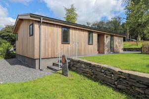 Una cabaña moderna de madera con un muro de contención de piedra, un camino de grava y un césped.