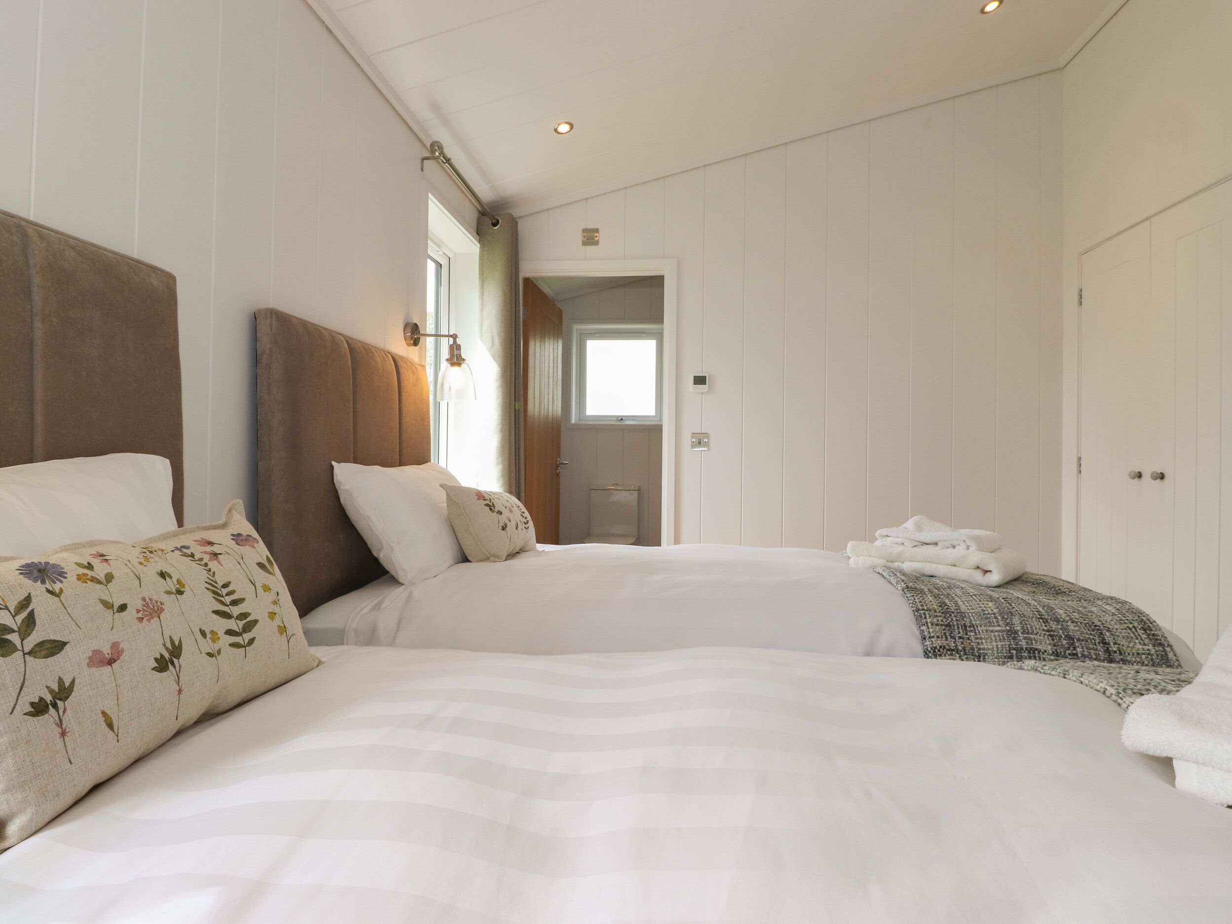 Un dormitorio con dos camas, ropa de cama blanca y cabecero de madera.