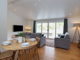 Una sala de estar moderna con una mesa de comedor de madera, sofás grises y un televisor montado en la pared.
