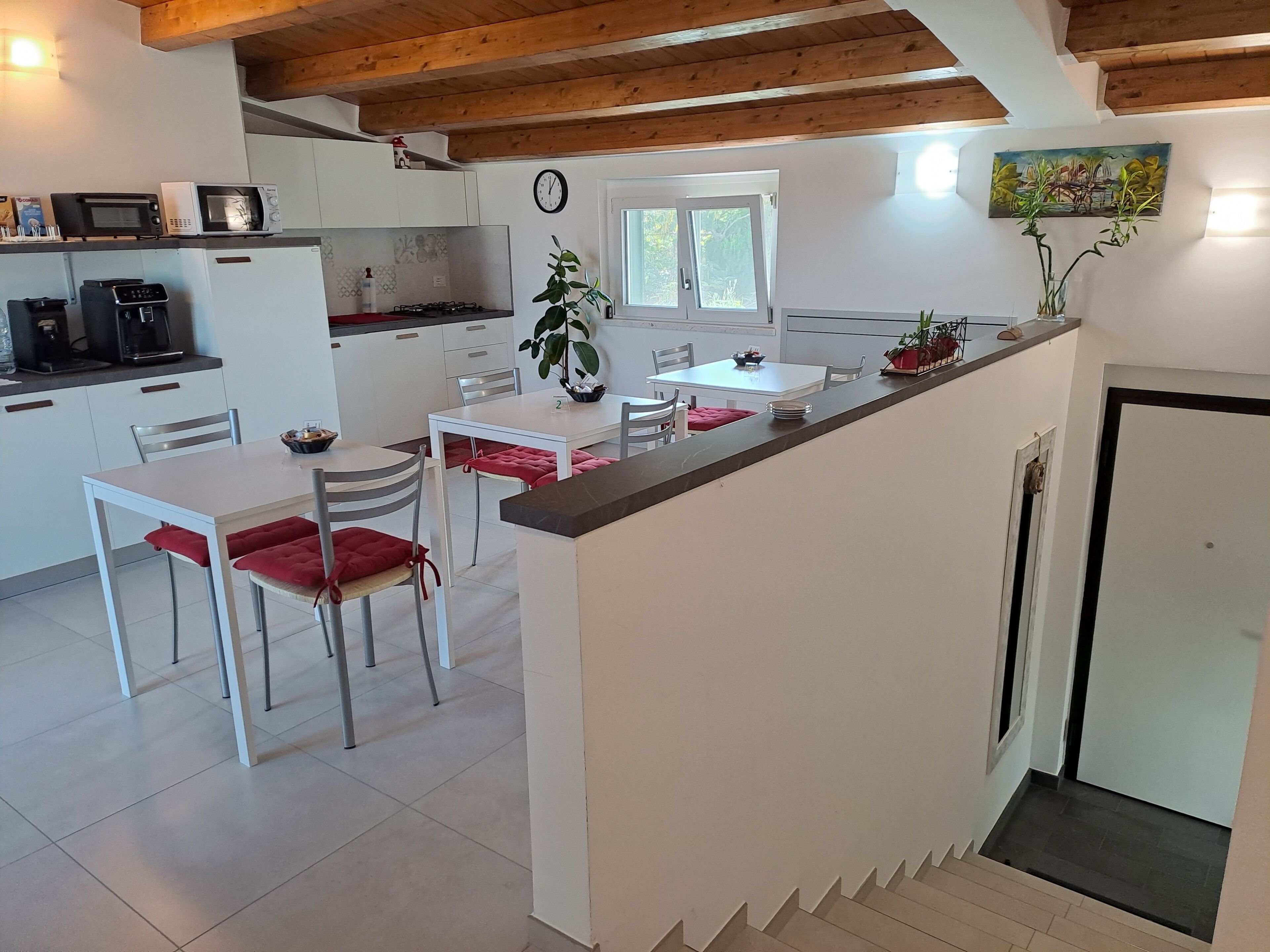 A modern kitchen with white cabinets, a dining area with red cushioned chairs, and a wooden ceiling.