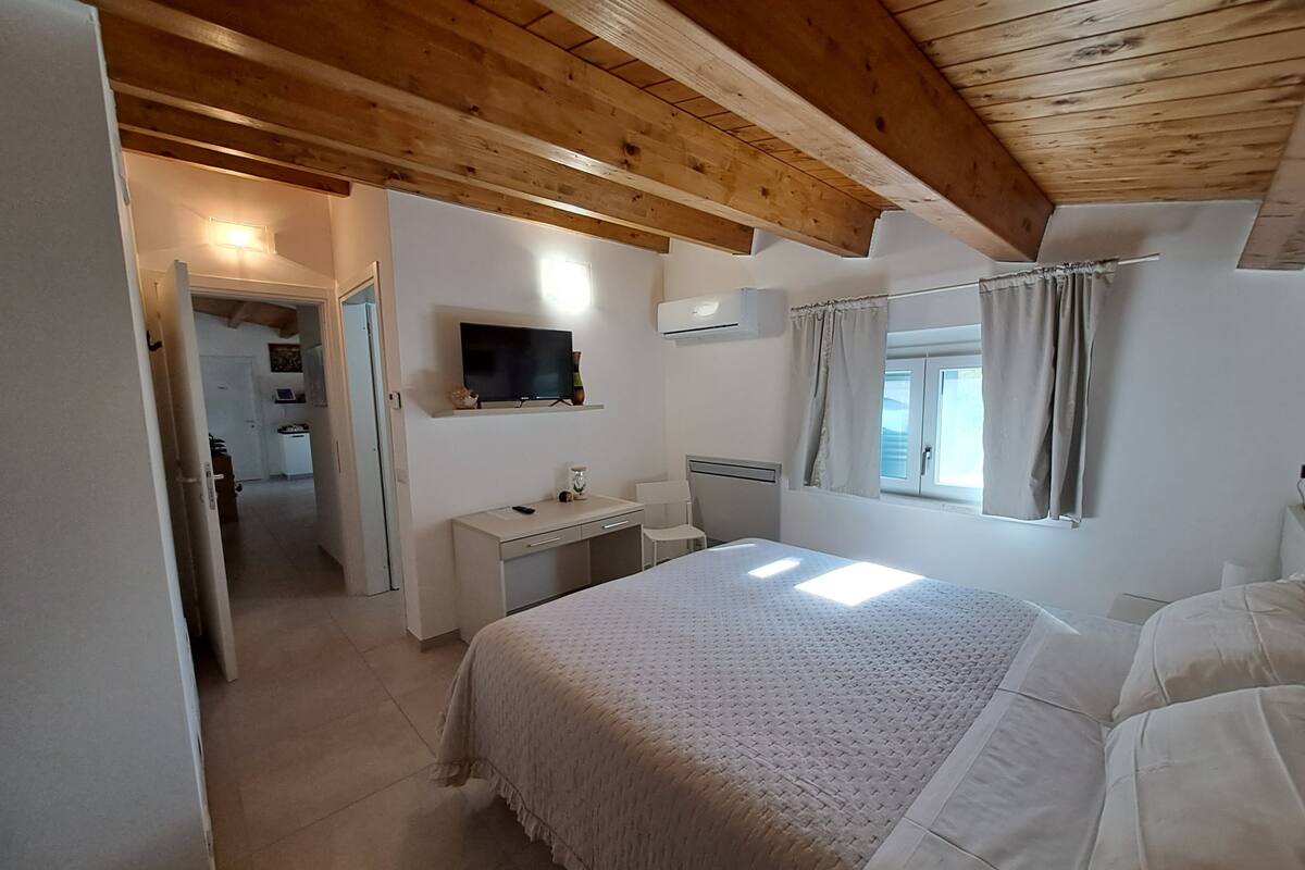 A bedroom with a bed, a desk, a television, and a window with curtains.