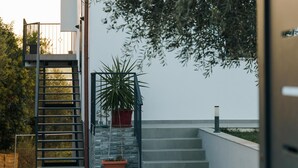 Un bâtiment moderne doté d’un escalier menant à un balcon, le tout entouré de verdure.