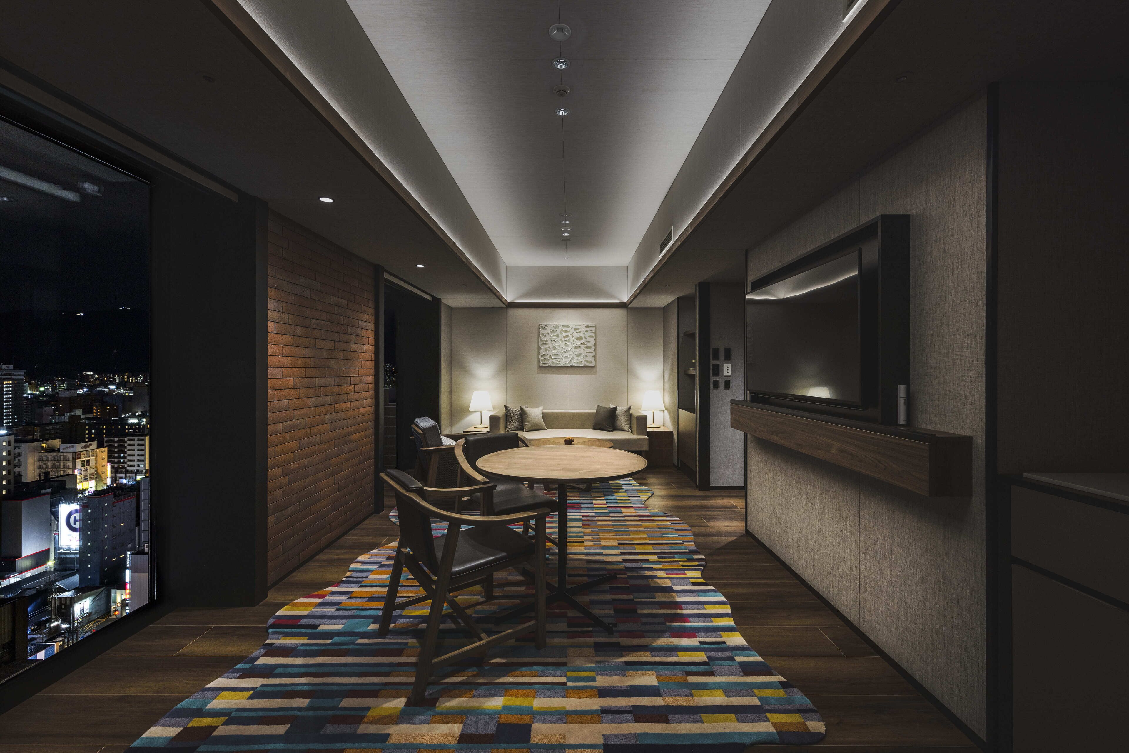 A modern hotel corridor with a round table and chairs, a sofa set, and a TV mounted on the wall.