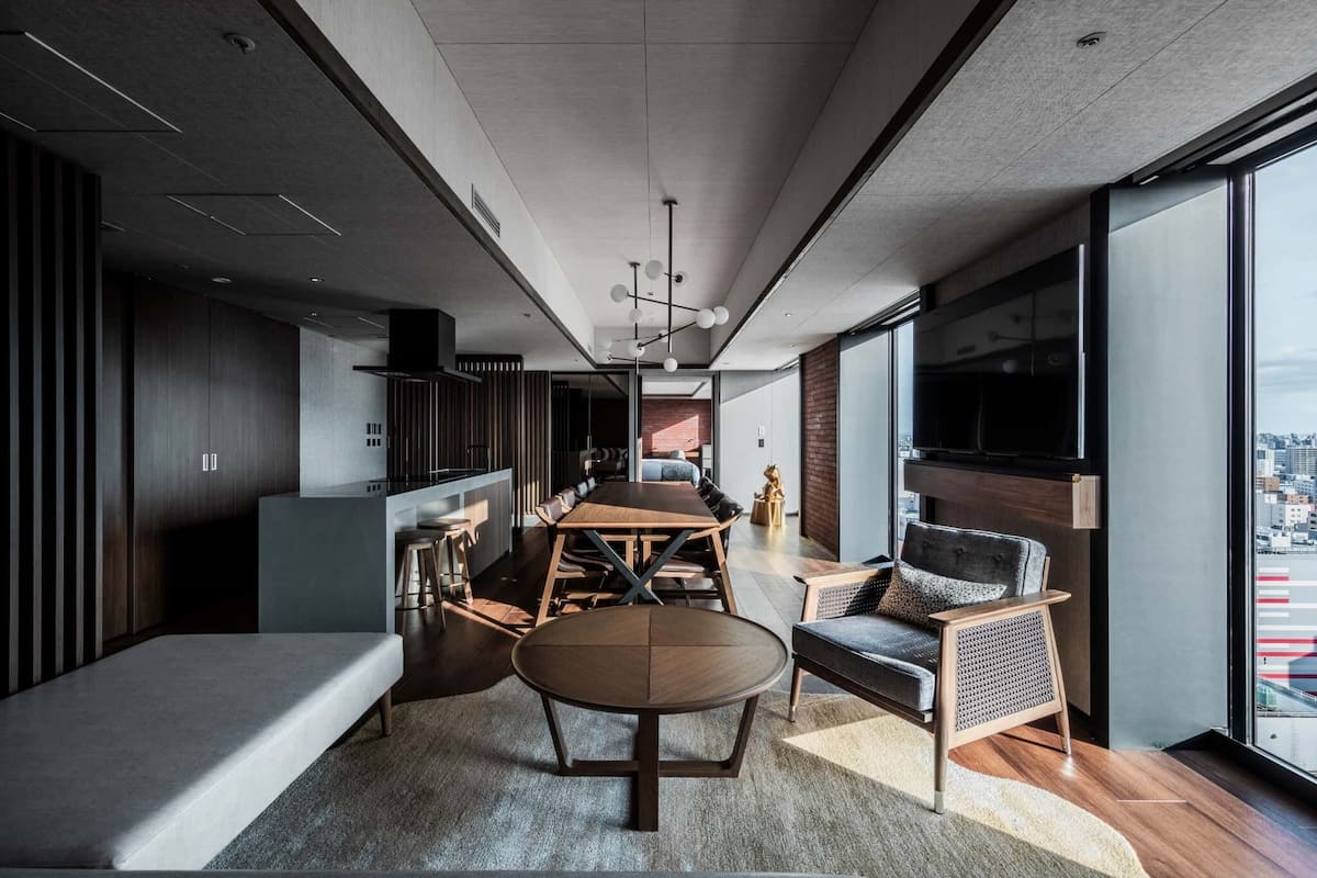 A modern interior with a dining area, seating, and a large window offering a city view.