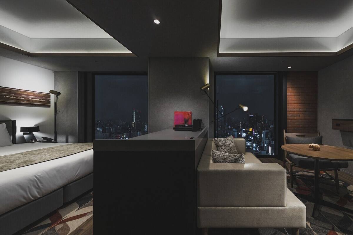 A modern hotel room with a sofa, a small table, a TV, and a city view.