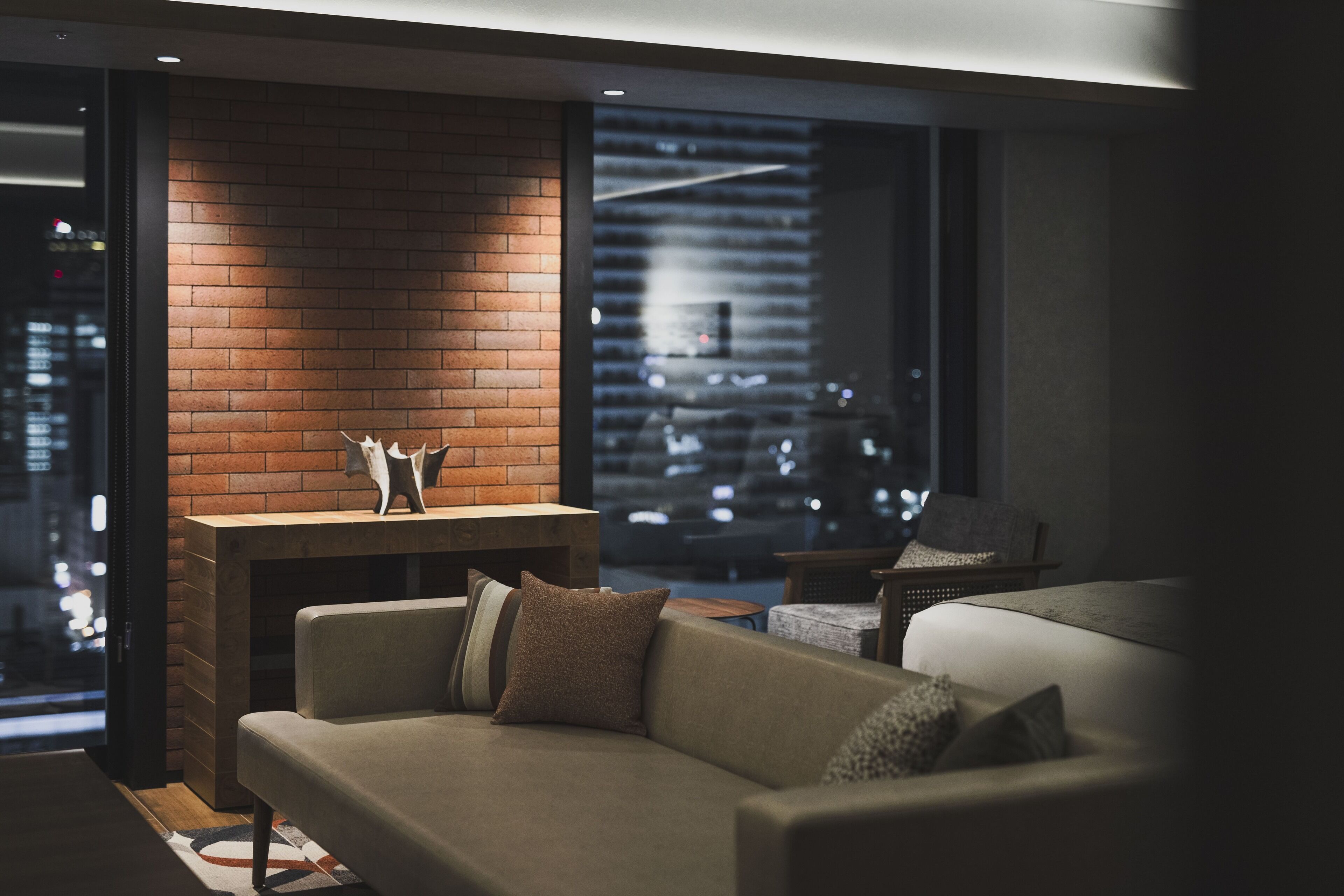 A modern living room with a brick fireplace, a sofa, and a view of a cityscape through large windows.