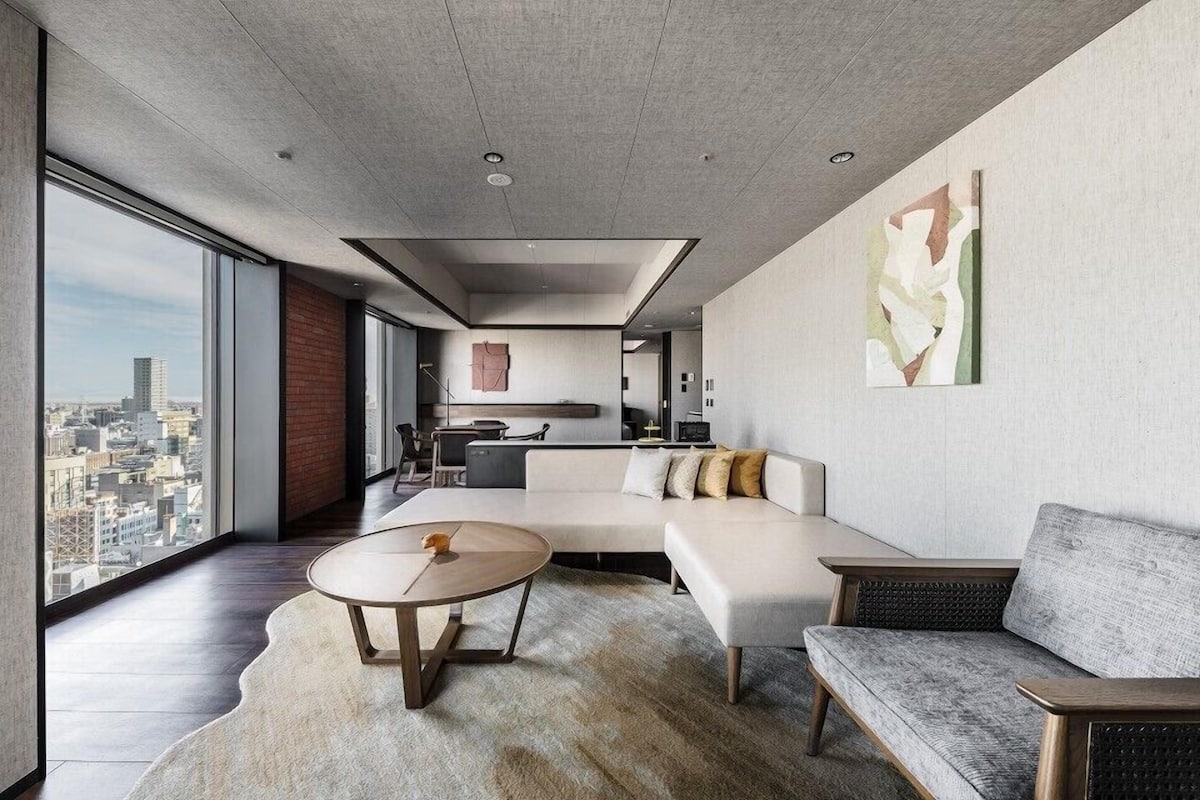 A modern living room with a large sofa, a round coffee table, and a view of the city through large windows.