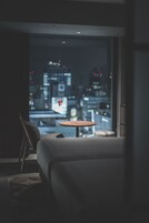 A modern hotel room with a large window offering a nighttime city view, a small round table, and a sofa.
