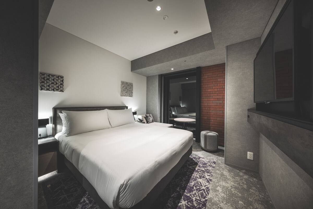A modern hotel room with a large bed, a small bathroom, and a TV.