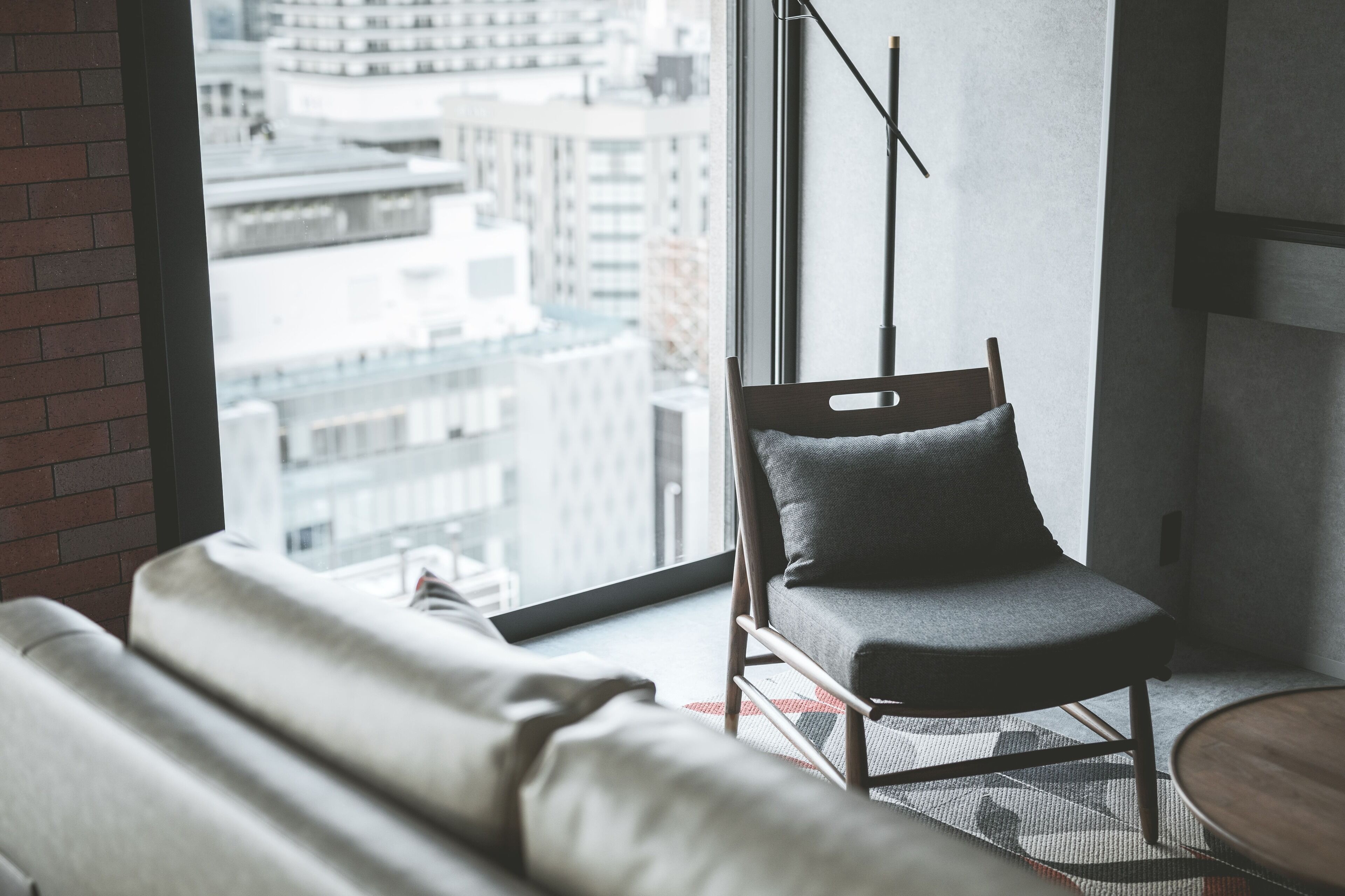 A modern room with a large window, a grey sofa, a wooden chair, and a small round table.