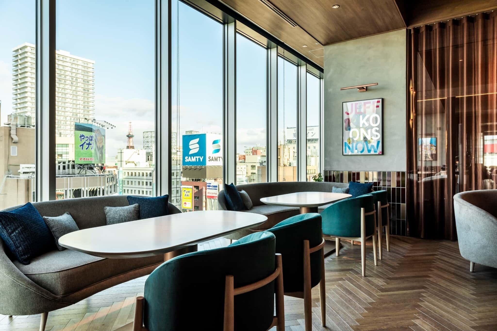A modern interior with large windows, a city view, and a seating area with tables and chairs.