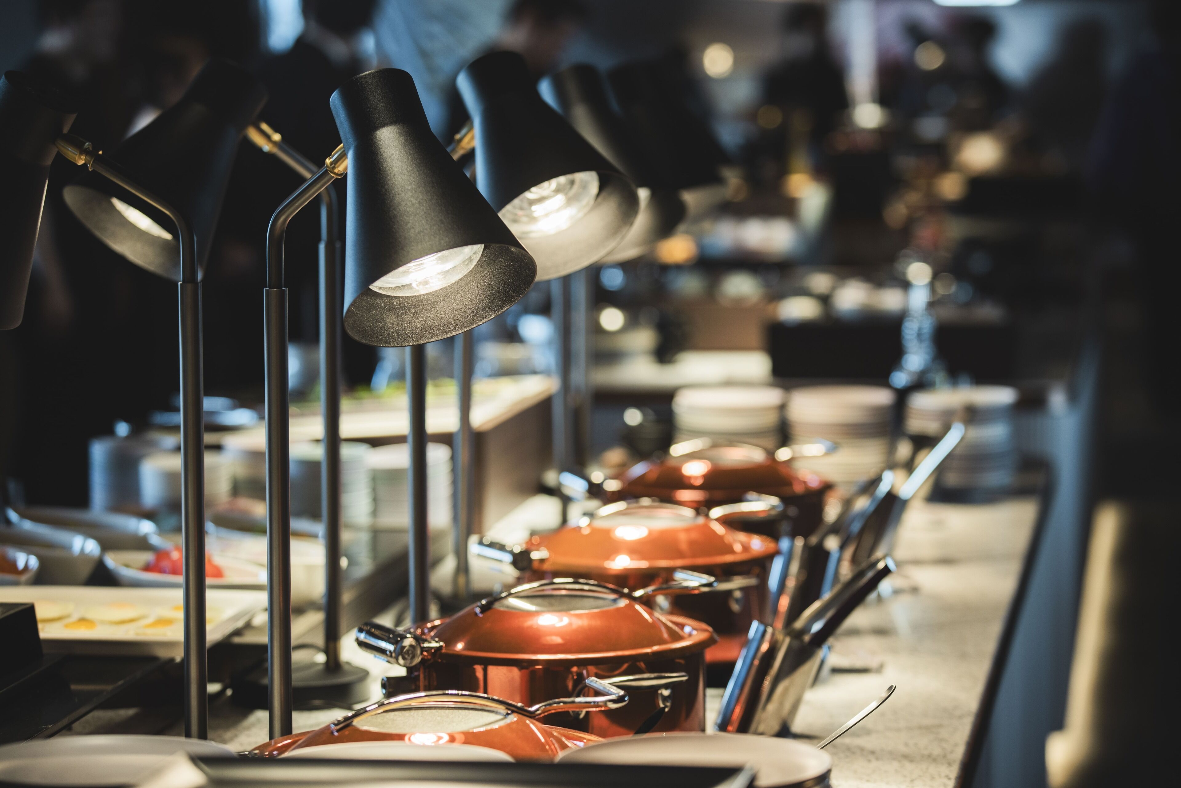 A buffet setup with multiple serving stations, each equipped with a black lamp and a set of utensils.