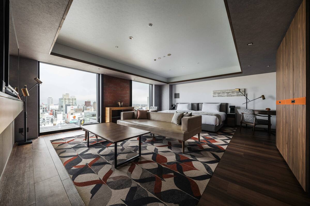 A modern hotel room with a large bed, a desk, and a view of the city.