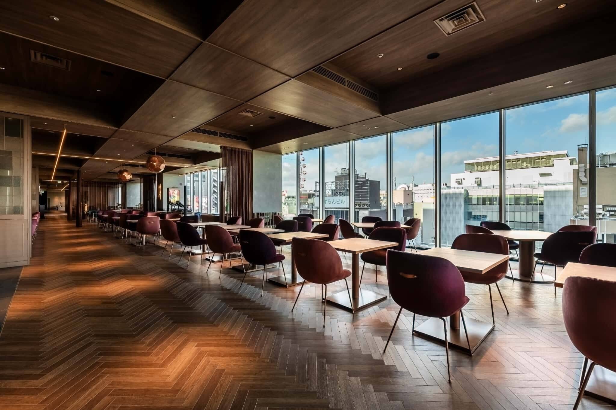 Un comedor moderno con suelo de madera, ventanas amplias y sillas rojas.