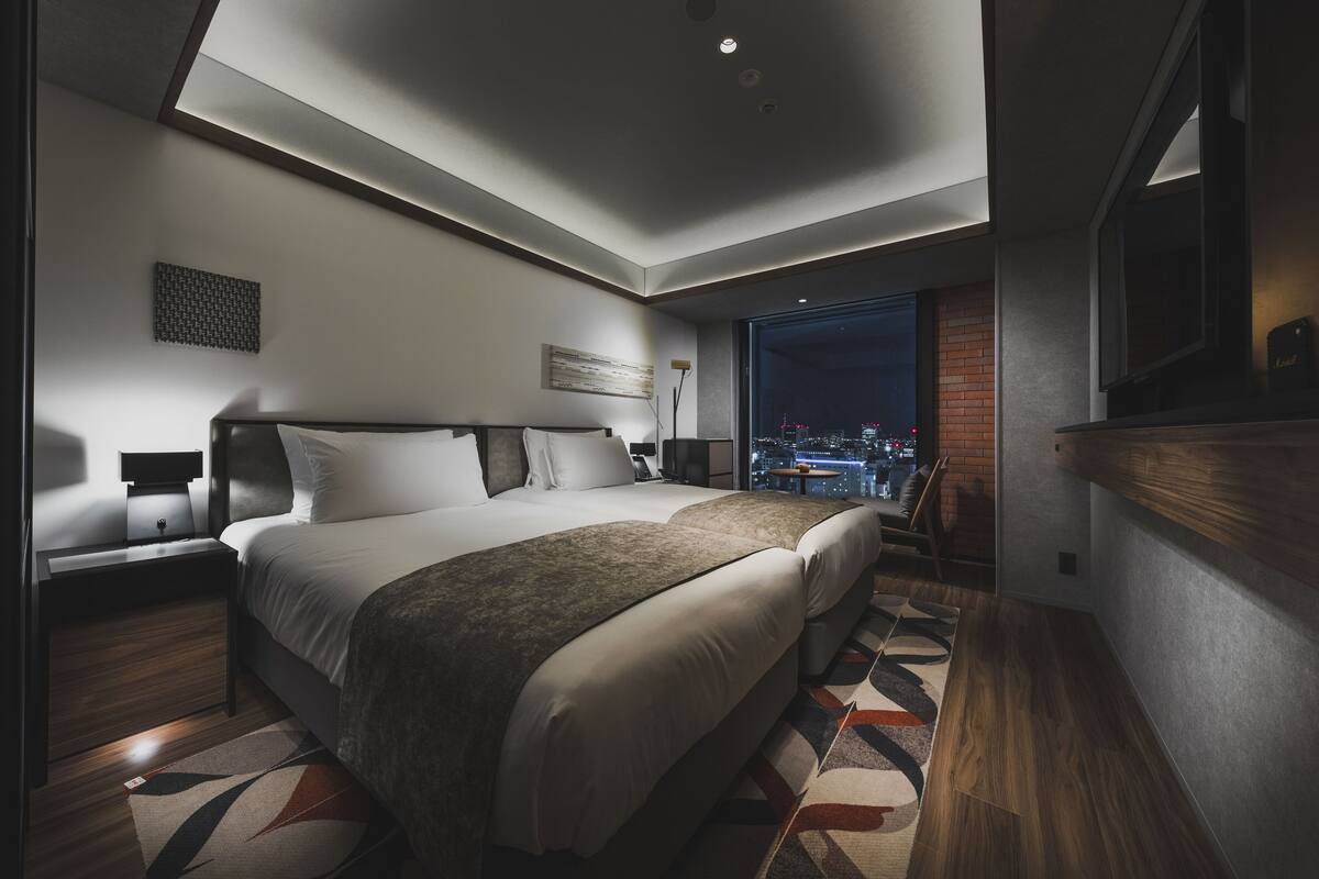 A modern hotel room with a large bed, a seating area, and a city view.