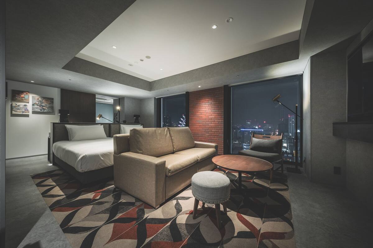 A modern hotel room with a bed, sofa, and a small dining table.