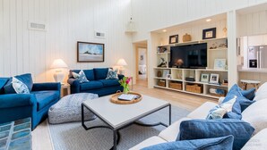 Amplia sala de estar con un conjunto de sofá azul, una mesa de centro y un televisor en un mueble blanco.