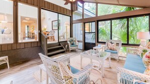 Una habitación amplia con muebles de mimbre, ventanas grandes y ventilador de techo.