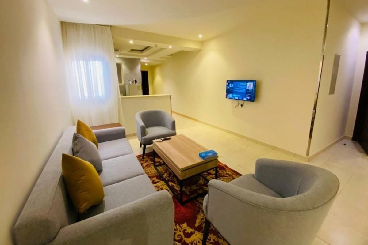 Un salon moderne comprenant un canapé, des fauteuils, une table basse et un téléviseur à écran plat fixé au mur.