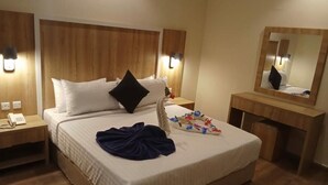 A hotel room with a large bed, wooden headboard, bedside lamps, a bedside telephone, a mirror, and a small table with a floral arrangement. - Towlan Khress Serviced Apartments (Riyadh)