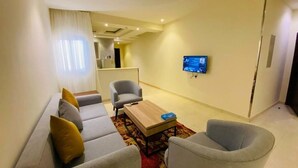 A modern living room with a sofa, armchairs, a coffee table, and a flat-screen TV mounted on the wall. - Towlan Khress Serviced Apartments (Riyadh)