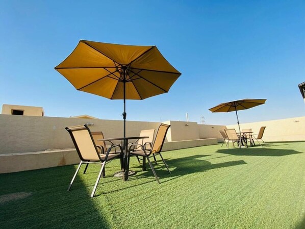 Un patio al aire libre con dos mesas y sillas, cada una con un paraguas amarillo.
