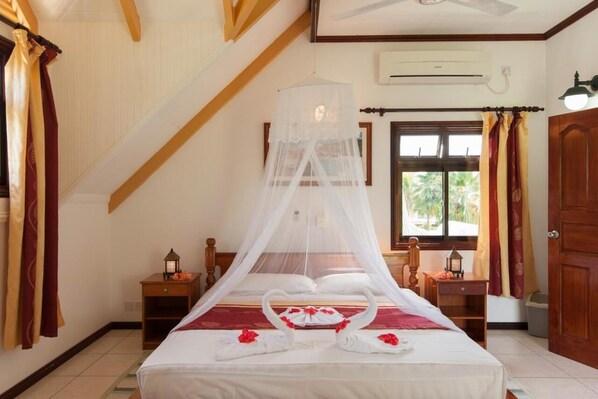 Un dormitorio con cama bajo dosel, dos mesitas de noche, una ventana con cortinas y una puerta.