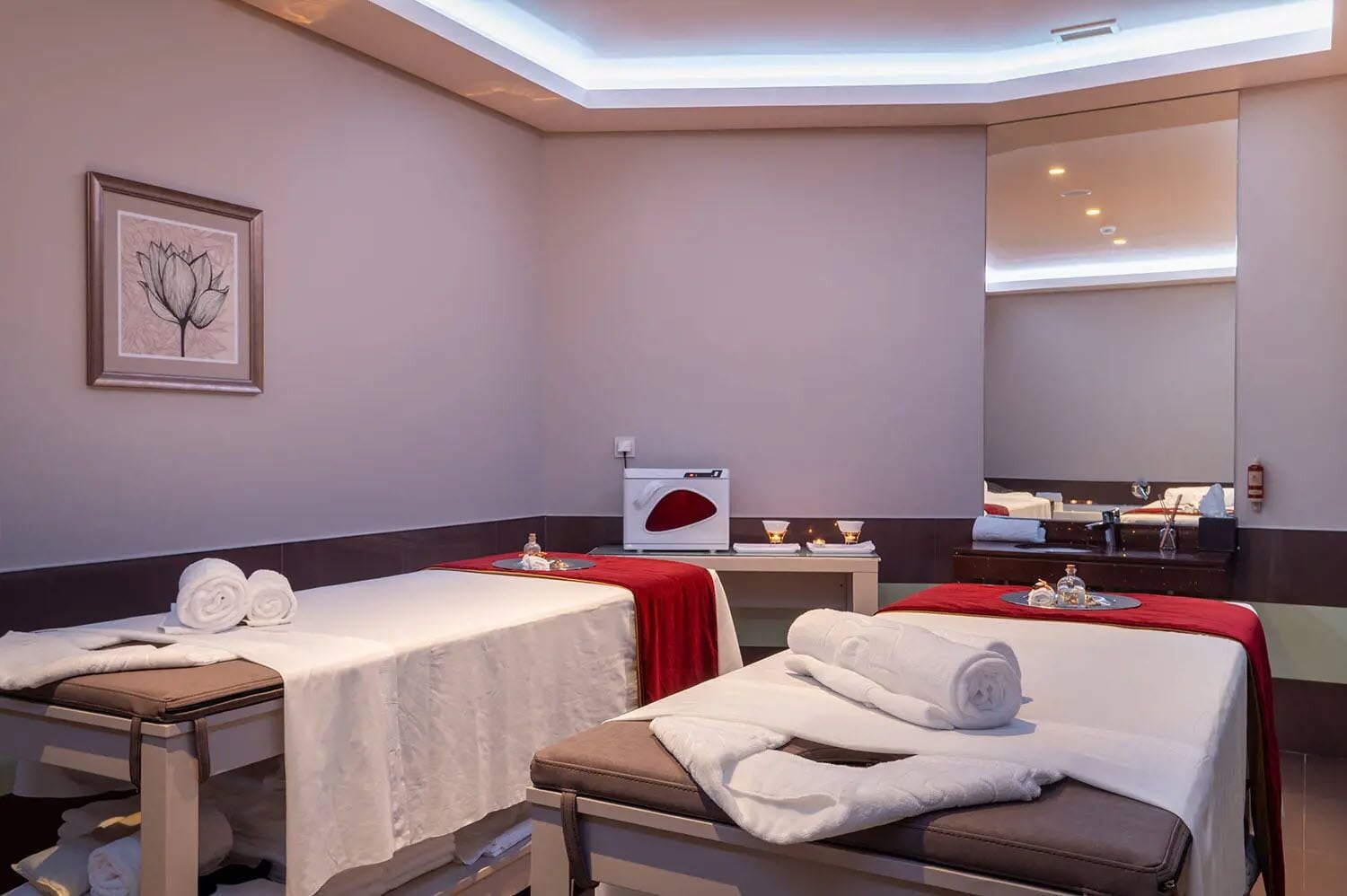 A hotel room with two beds, a desk, a mirror, and a framed artwork on the wall.