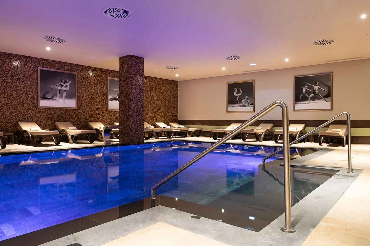 A swimming pool with lounge chairs, a central pillar, and framed pictures on the walls.