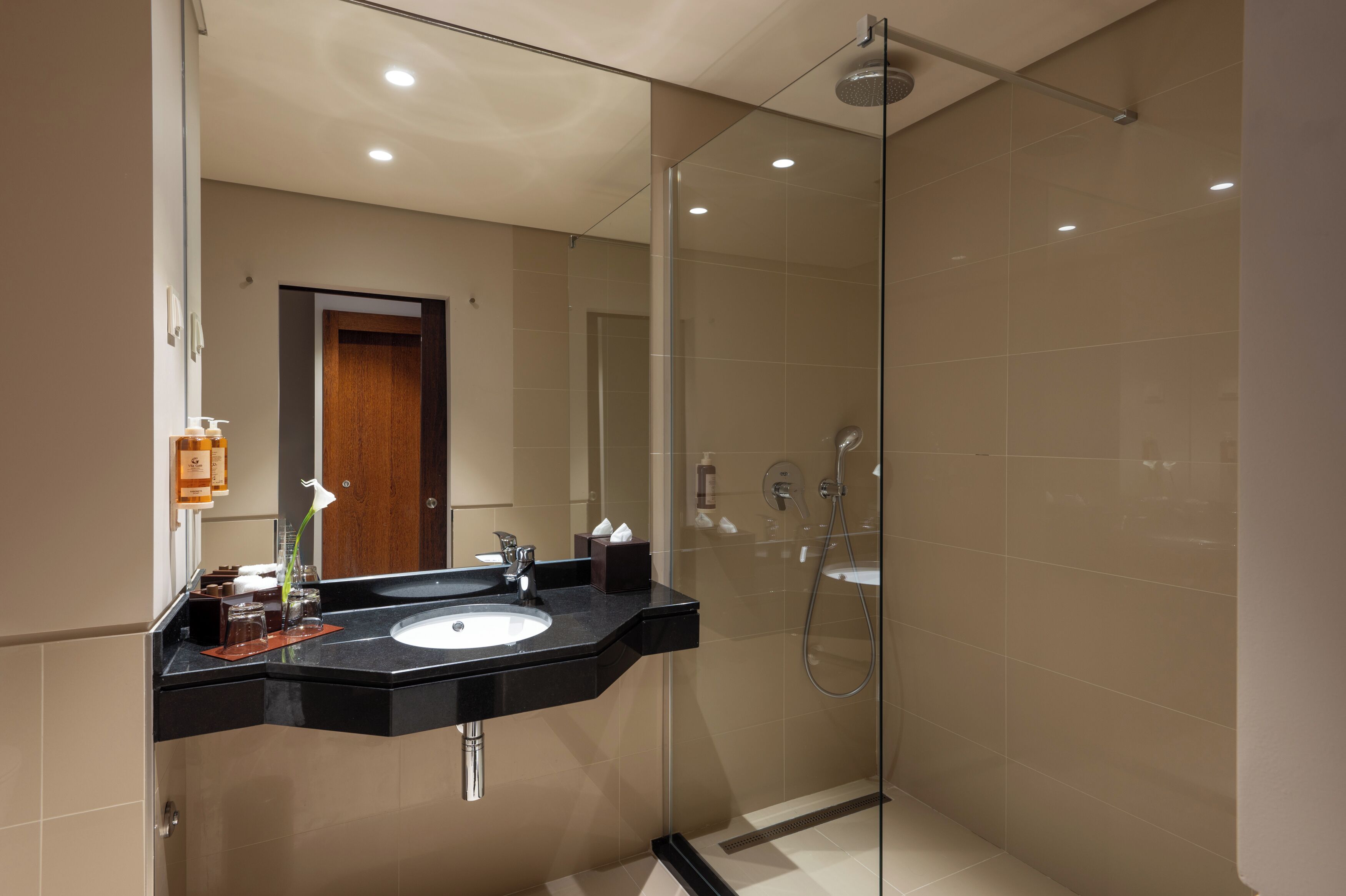 A modern bathroom with a glass-enclosed shower, a black countertop sink, and a wooden door.