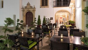 An outdoor dining area with wicker tables and chairs, potted plants, and a stone archway. - Vila Gale Collection Tomar Hotel (Tomar)