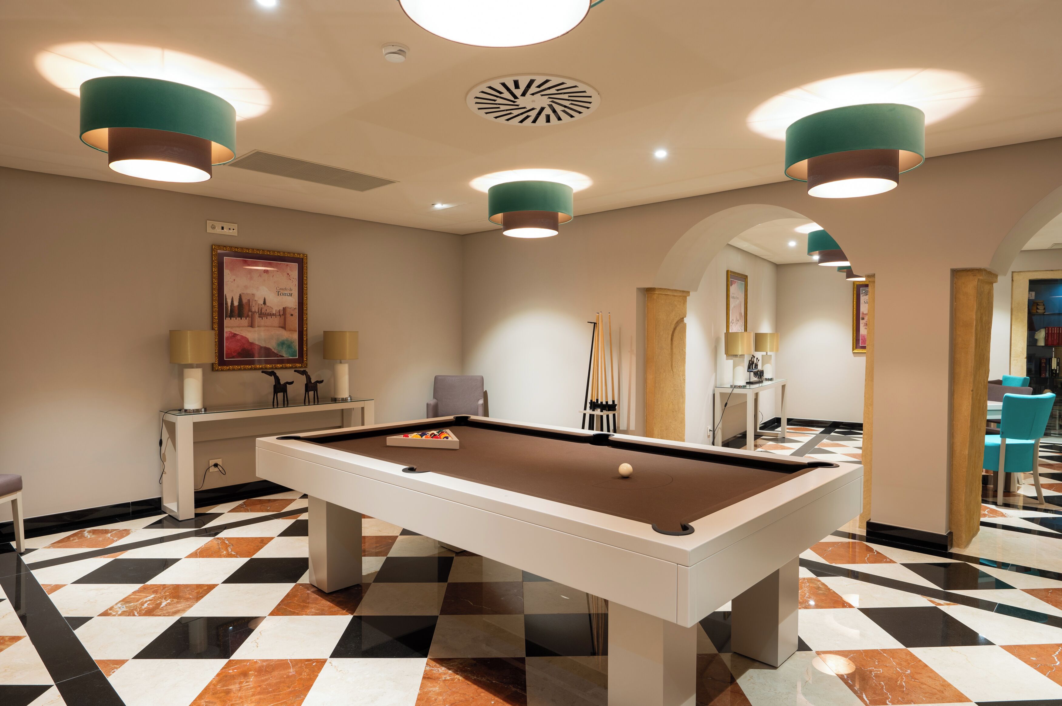 A pool table in a room with a checkered floor, recessed lighting, and a framed picture on the wall.