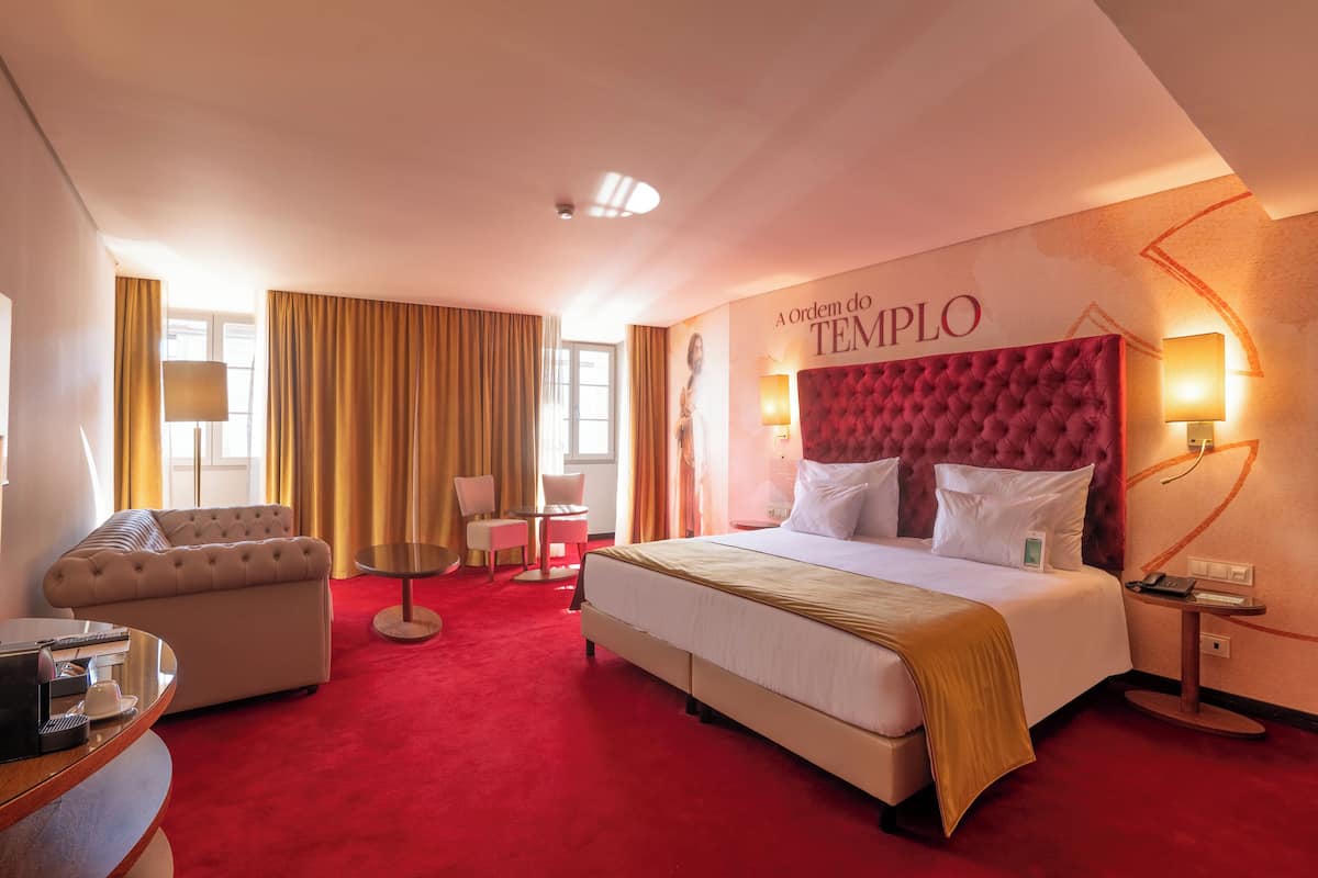 Quarto de hotel com uma cama grande, um sofá, uma escrivaninha e uma cadeira.