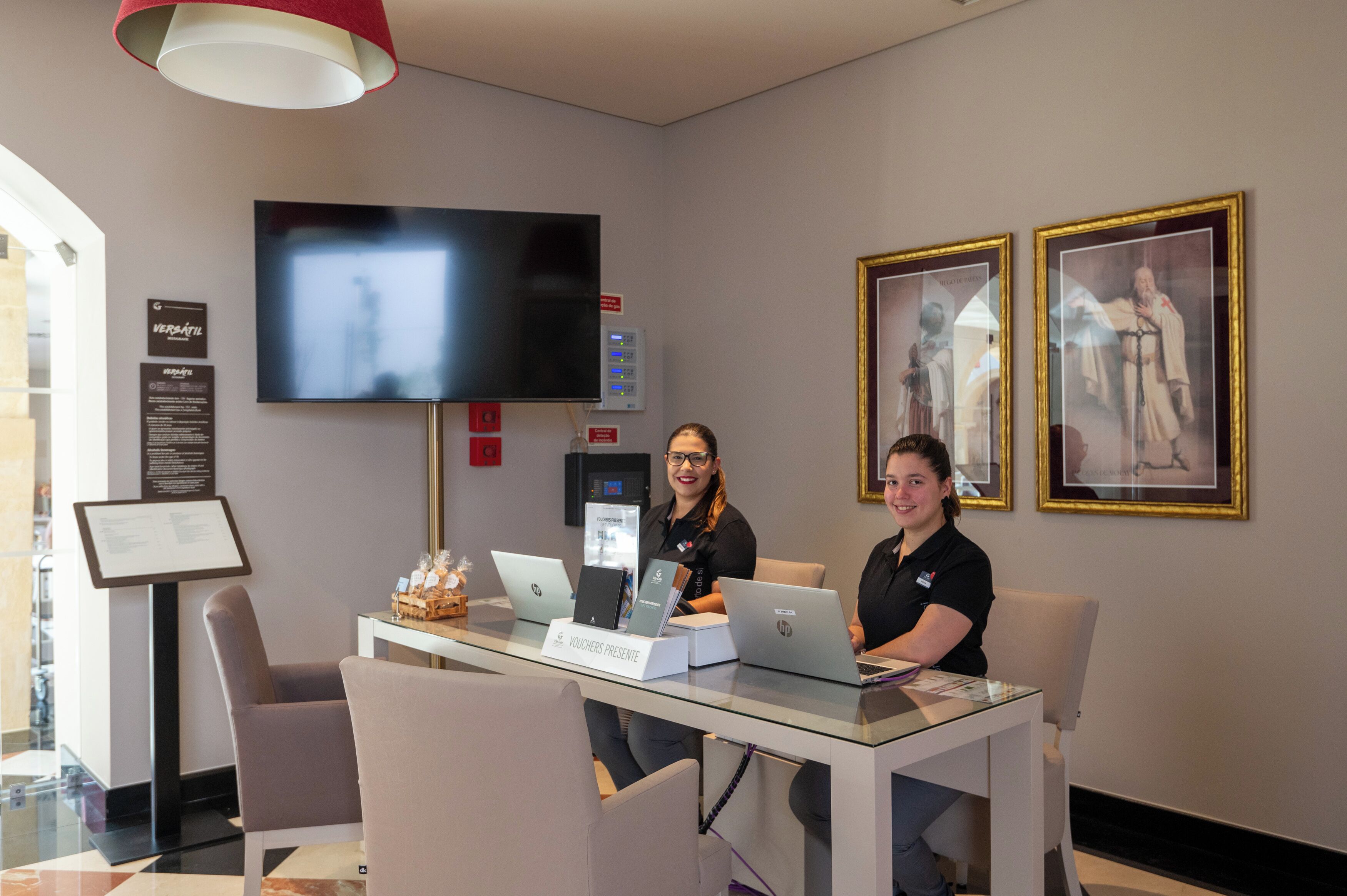 A reception area with a flat-screen TV, framed pictures on the wall, and two people at a desk with laptops.