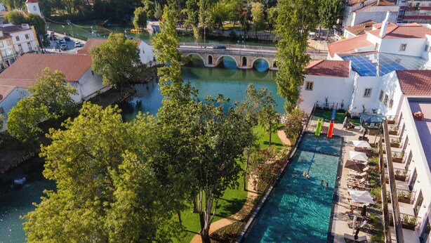 A rooftop pool with lounge chairs, a bridge over a river, and surrounding greenery. - Vila Gale Collection Tomar Hotel (Tomar)