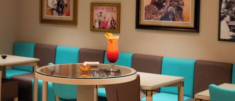A restaurant with turquoise and brown seating, a round table with a glass top, and framed posters on the wall.