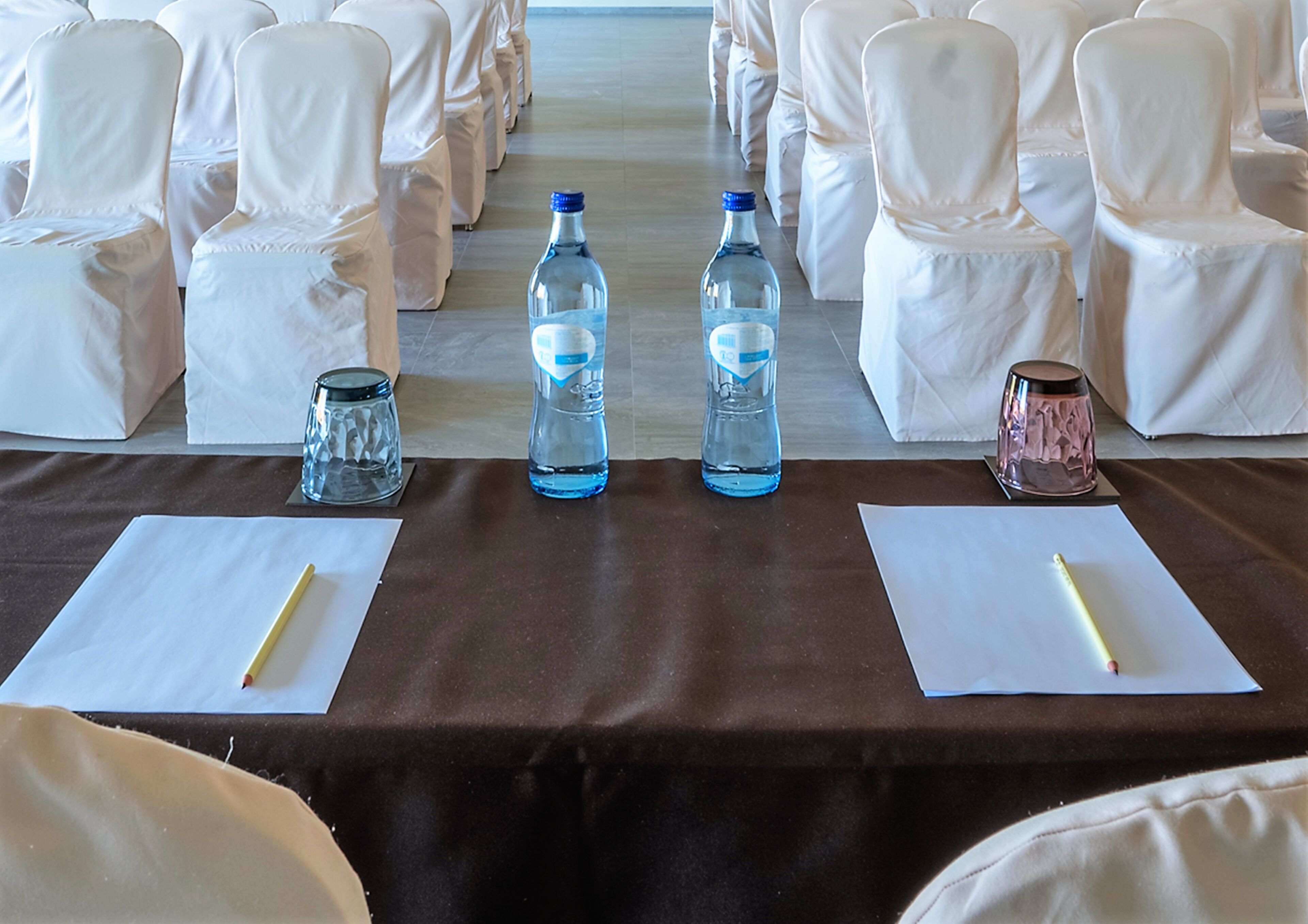 A table set for a meeting or event with two chairs, two water bottles, a glass, and a pen on a brown tablecloth.