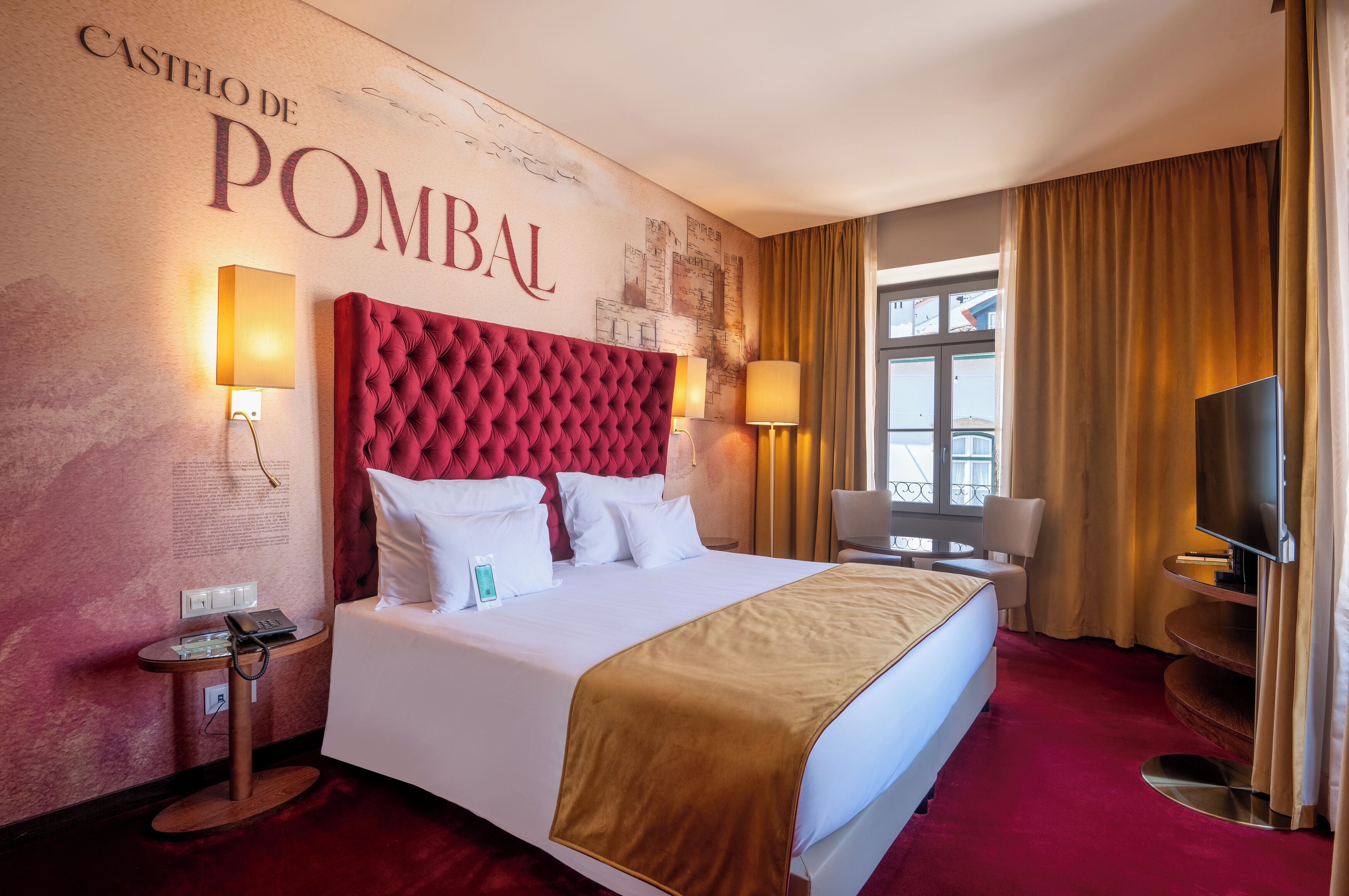 Una habitación de hotel con una cama grande, dos mesitas de noche, un televisor y una ventana con cortinas.