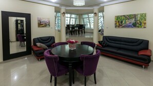 Ein modernes Wohnzimmer mit einem runden Esstisch, violetten Stühlen, einem schwarzen Sofa und einem großen Spiegel.