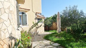 A stone pathway leading to a building with a tiled roof and a window with shutters.