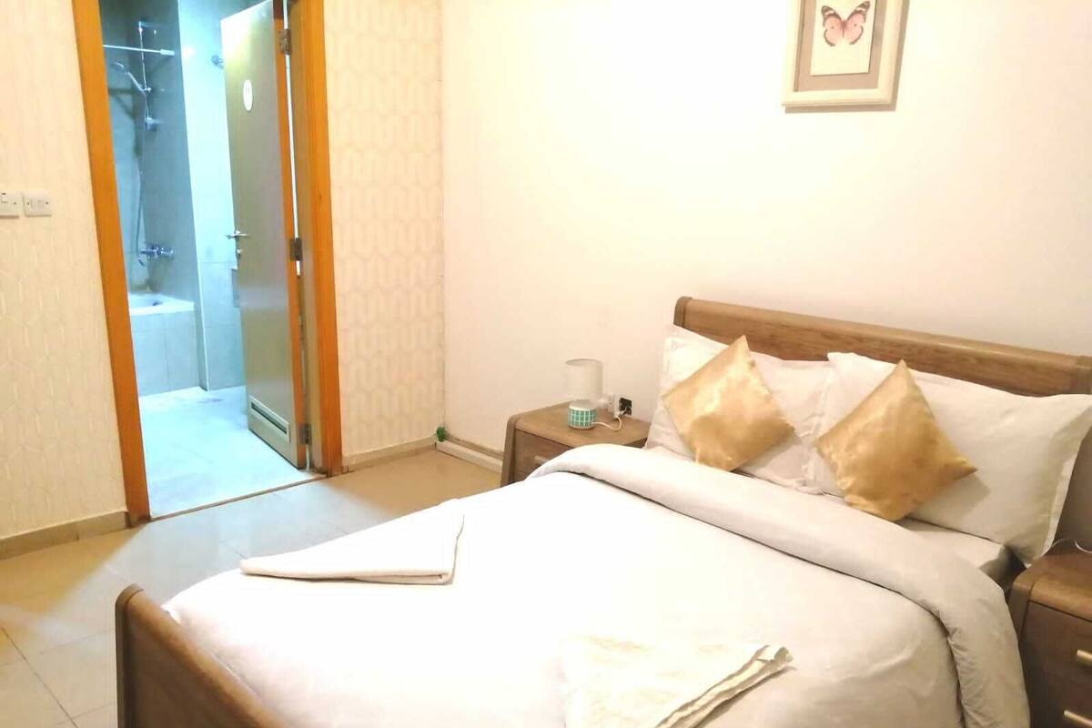 A hotel room with a bed, a nightstand, a bedside table, a framed picture on the wall, and a bathroom visible through an open door.