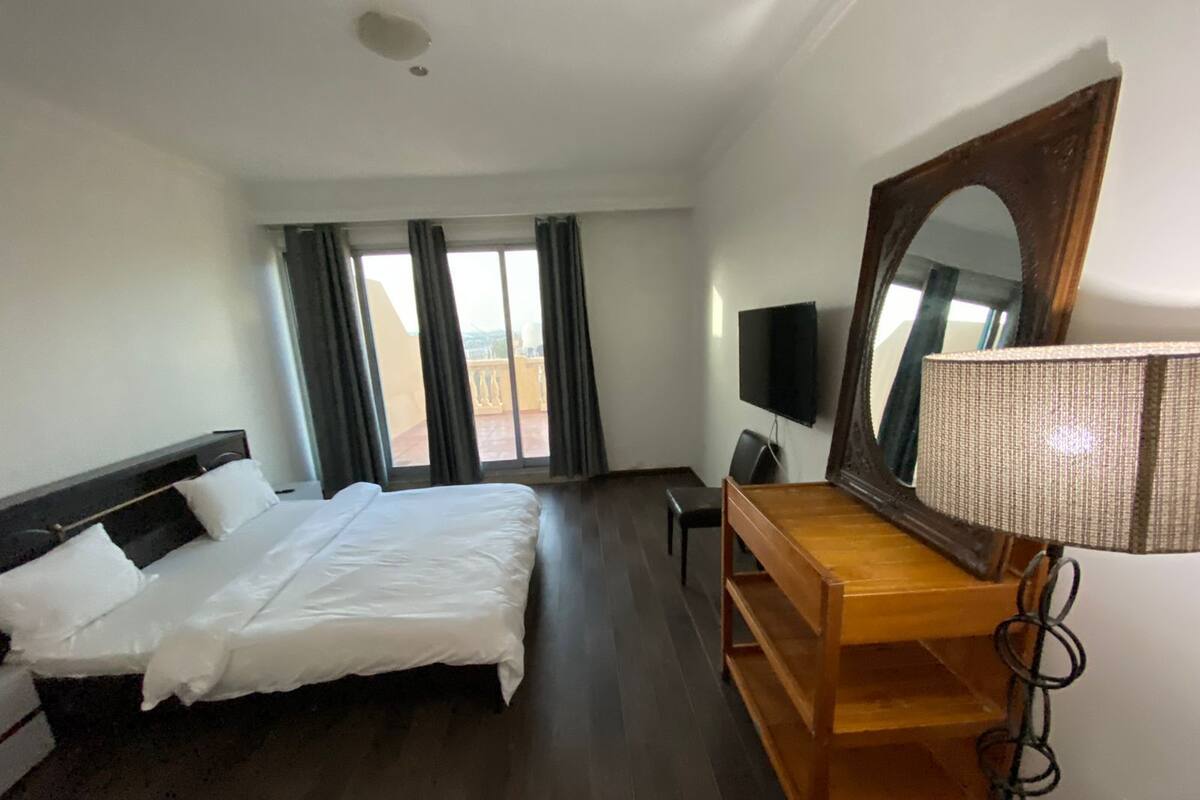 A hotel room with a bed, a desk, a chair, a TV, and a large mirror.
