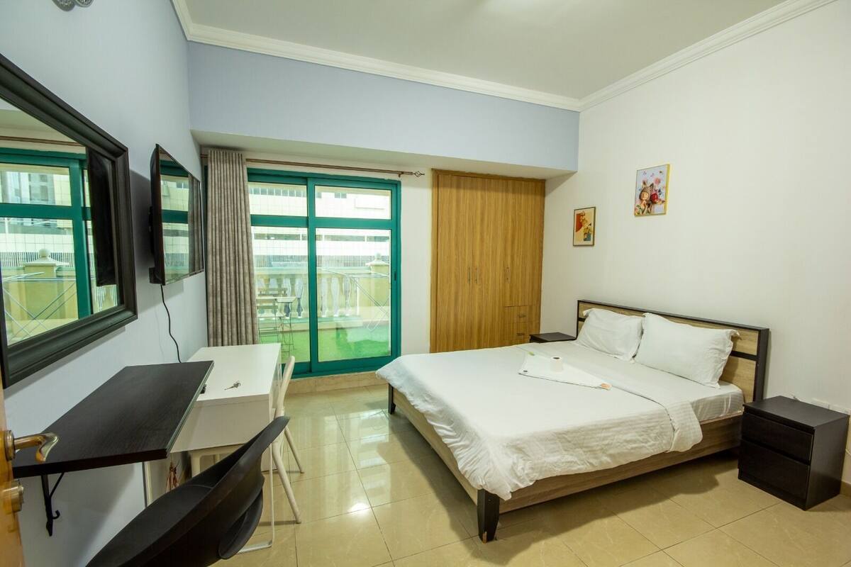 A hotel room with a bed, a desk, a chair, a TV, a wardrobe, and a balcony with a view.
