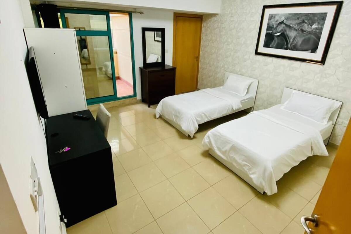 A hotel room with two beds, a desk, a mirror, a framed picture on the wall, and a ceiling light fixture.
