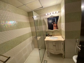 Un baño con cabina de ducha de vidrio, tocador con lavamanos y espejo con luces superiores.