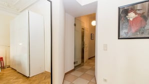 A hallway with a white wardrobe, a glass door leading to a bathroom, and a framed painting on the wall.