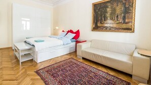 A bedroom with a bed, a white sofa, a small table, a painting, and a patterned rug.