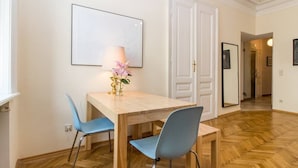A dining area with a wooden table, two blue chairs, a vase with flowers, and a framed picture on the wall.