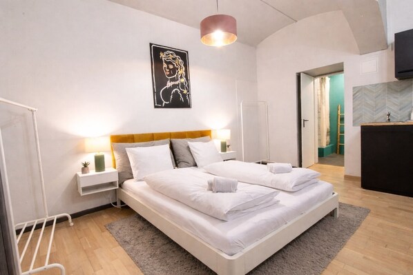 A double bed with white linens, a headboard, bedside tables with lamps, a wall-mounted artwork, and a wooden floor.